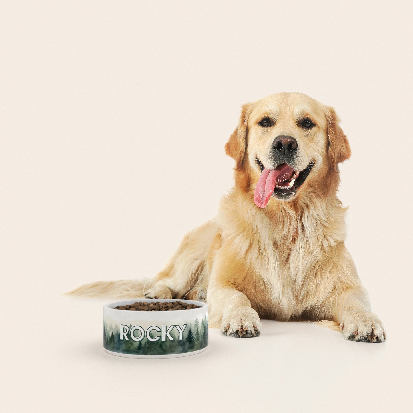 Un golden retriever assis à côté d'un bol pour chien au motif Sapins personnalisé avec le nom ROCKY
