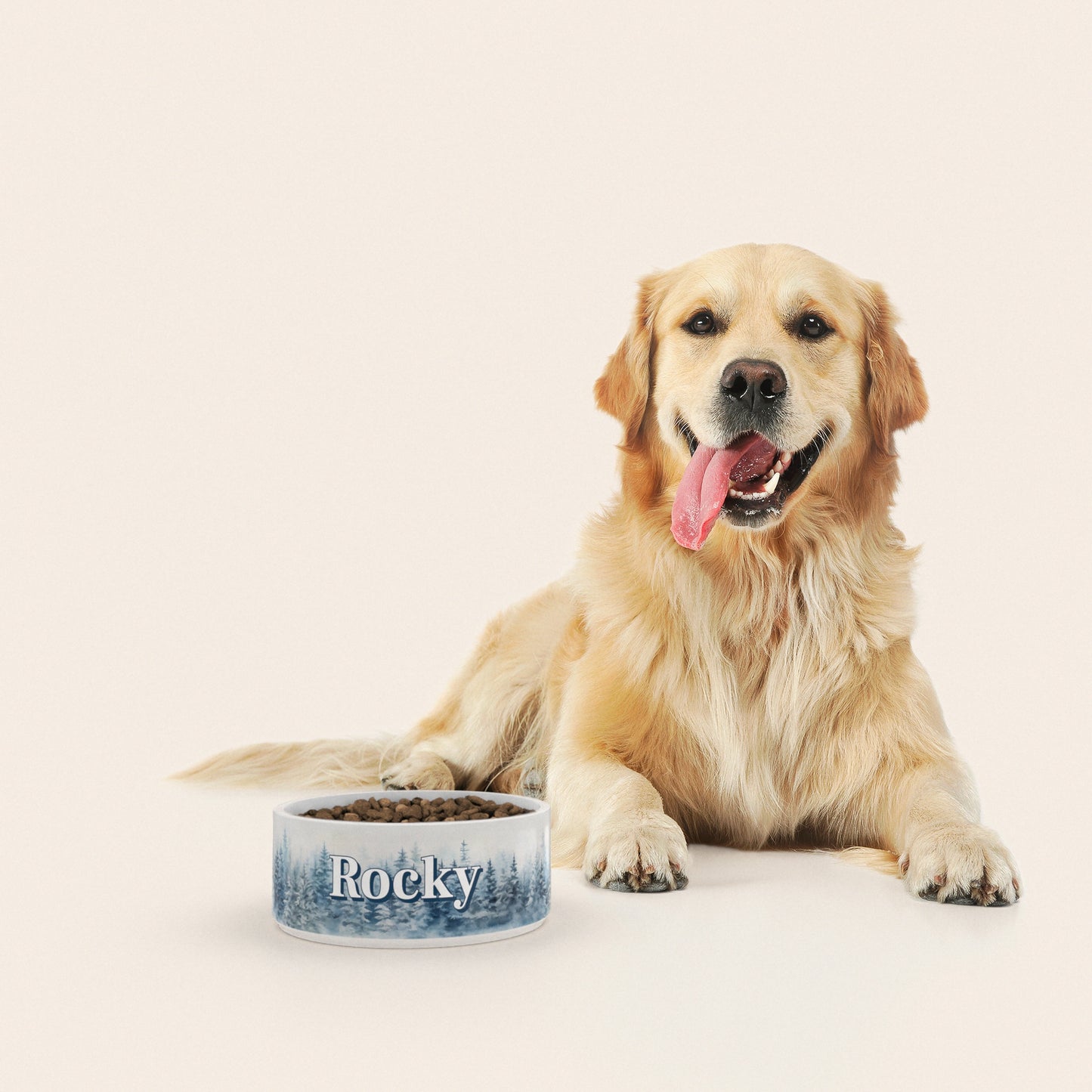 Un golden retriever assis à côté d'un bol pour chien au motif Sapins Enneigés personnalisé avec le nom ROCKY