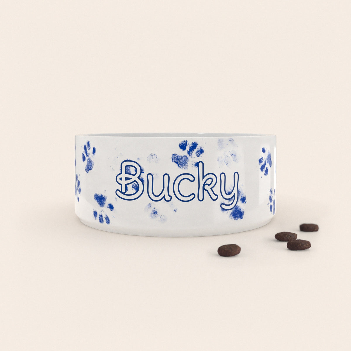Gamelle pour chien au motif Pattes Bleues personnalisés avec le nom Bucky, accompagné de croquettes sur fond neutre.