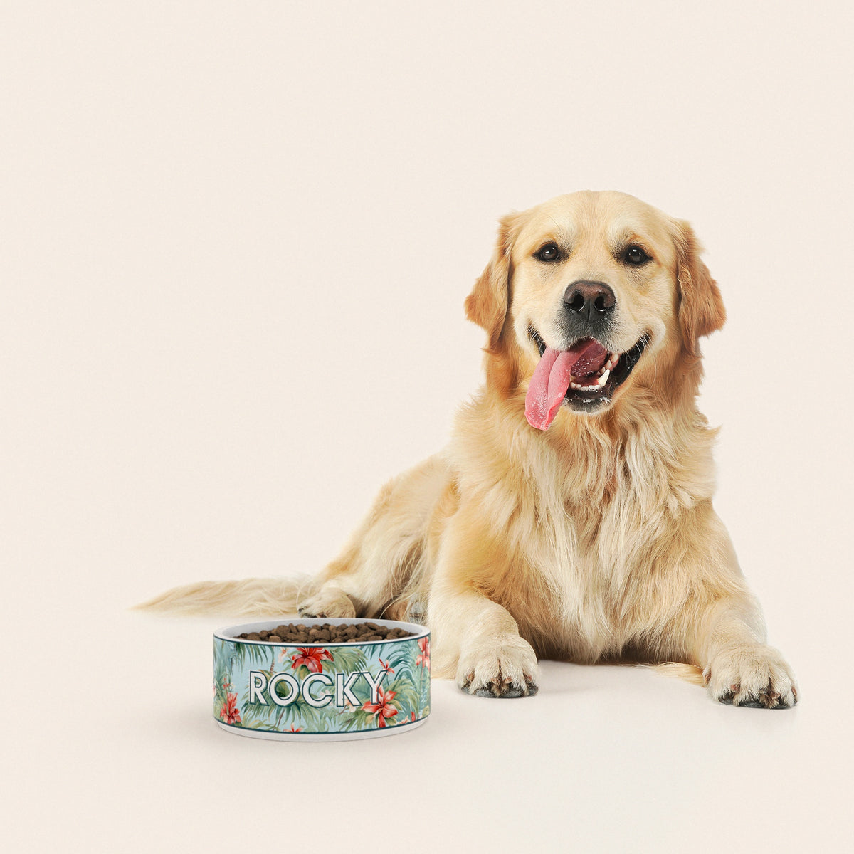 Un golden retriever assis à côté d'un bol pour chien au motif Hawaï personnalisé avec le nom ROCKY